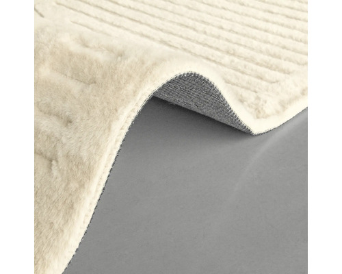 Detaliu al unui covor de culoare deschisă, cu o textură țesută și un colț ondulat care arată partea inferioară