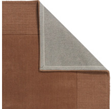 Vizualizare detaliată a unui covor maro cu un colț îndoit care arată partea inferioară gri