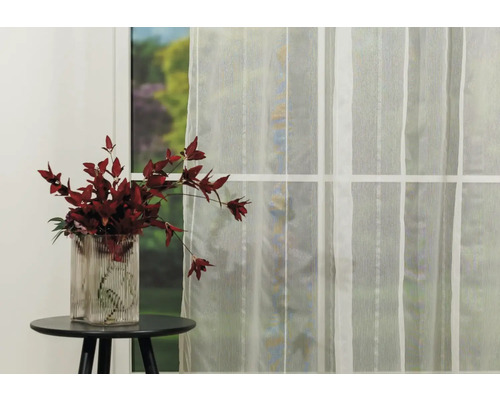 Cortină decorativă în fața unei ferestre, lângă care se află o vază cu flori pe o masă