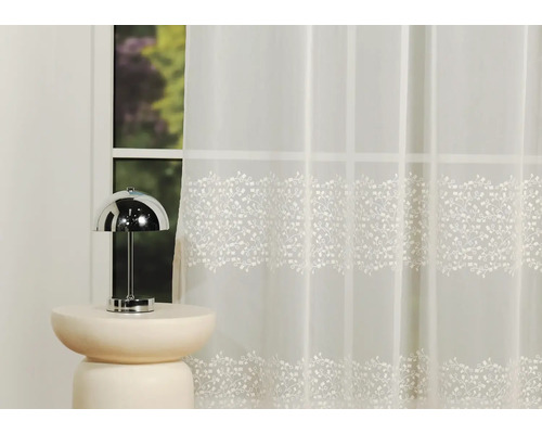 Șaluri decorative din voal cu model floral în fața unei ferestre.