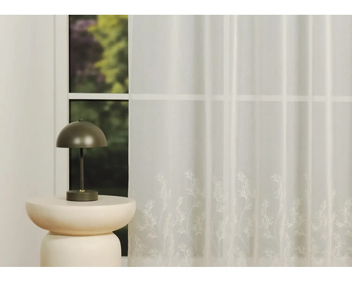 Perdea decorativă, transparentă, cu motiv floral în fața unei ferestre și a unei lămpi.