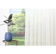 Plantă de interior în ghiveci albastru pe o măsuță laterală aurie în fața unei ferestre cu perdea.