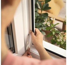 O persoană montează o etanșare de fereastră pe un cadru alb de fereastră.