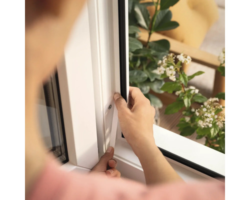 O persoană montează o etanșare de fereastră pe un cadru alb de fereastră.