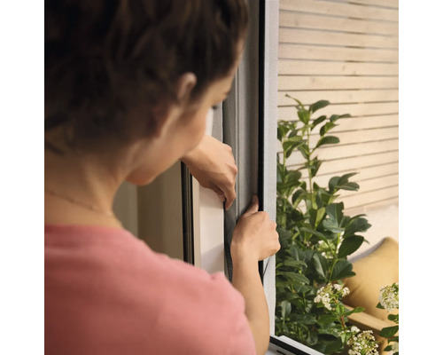 Femeie instalează o plasă de țânțari pe fereastră.