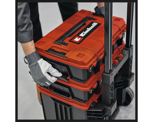 Cutii pentru scule sistem Einhell E-Case stivuite pe un cărucior, ținute de o mână cu mănușă de protecție.