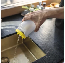 O persoană toarnă apă dintr-un recipient de plastic alb cu capac galben într-o chiuvetă de bucătărie aurie.