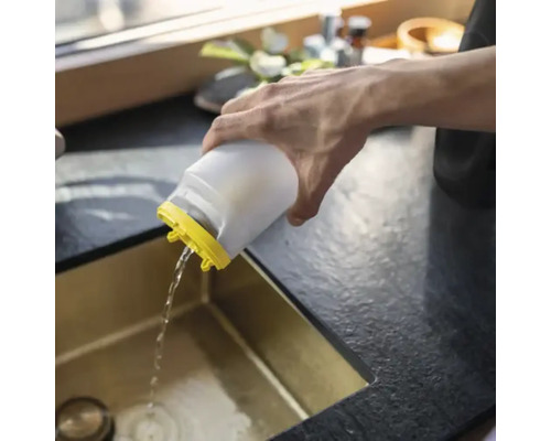 O persoană toarnă apă dintr-un recipient de plastic alb cu capac galben într-o chiuvetă de bucătărie aurie.