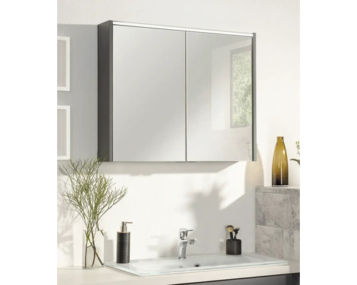Dulap cu oglindă cu două uși deasupra unei chiuvete deschise la culoare într-o baie modernă, cu dozator de săpun și baterie.