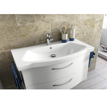 Mască de chiuvetă albă cu două sertare curbate și lavoar din ceramică în fața unui perete cu plăci din piatră naturală bej.