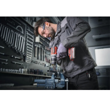 Un meseriaș găurește o piesă metalică cu o mașină de găurit cu acumulator într-un atelier cu un perete de scule organizat.
