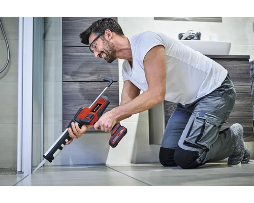 Un meșter folosește un pistol de silicon Einhell cu acumulator pentru a etanșa profesional îmbinarea unei cabine de duș în baie.