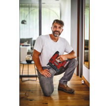 Meșter îngenuncheat pe o podea de lemn, ținând un capsator cu acumulator Einhell, într-un interior modern.