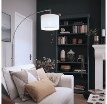 Lampadar arc modern cu abajur textil și cadru metalic într-un living confortabil cu bibliotecă și șemineu.