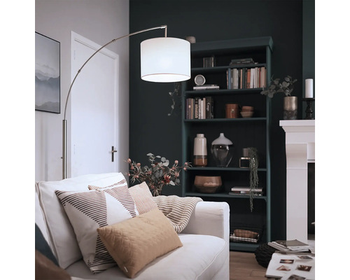 Lampadar arc modern cu abajur textil și cadru metalic într-un living confortabil cu bibliotecă și șemineu.