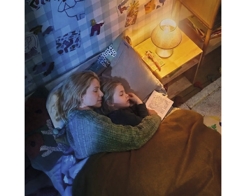 Mama și copilul citesc împreună o carte în camera copiilor la lumina caldă a unei veioze.