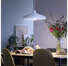 Lampă suspendată modernă deasupra unei mese de sufragerie într-o cameră luminoasă, cu un buchet de flori și decorațiuni.