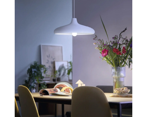 Lampă suspendată modernă deasupra unei mese de sufragerie într-o cameră luminoasă, cu un buchet de flori și decorațiuni.