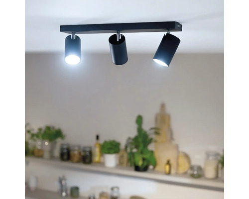 Spot de tavan cu trei surse de lumină cilindrice pe o bară dreptunghiulară pentru iluminare directă într-un spațiu de locuit.