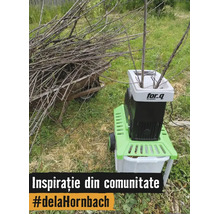 Un tocator de gradina electric For Q marunteste crengi intr-o gradina langa o roaba plina cu resturi vegetale.