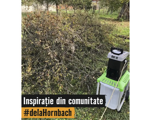 Un tocător de grădină electric marca for_q stă lângă o grămadă mare de ramuri și resturi vegetale pe o peluză.