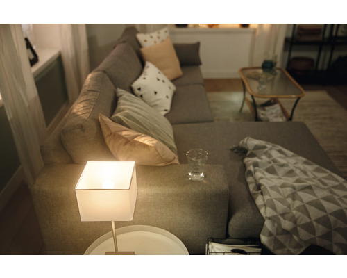 Cameră de zi cu canapea de colț gri, perne, lampă de masă și măsuță laterală