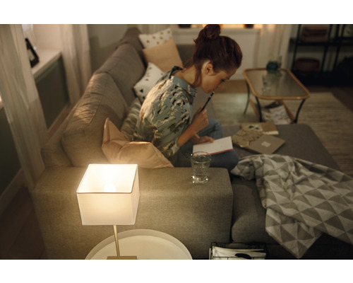 Femeie stând pe o canapea și scriind notițe lângă o lampă de masă într-o sufragerie.