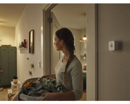 Femeie cu coș de rufe pe hol cu senzor de mișcare pe perete