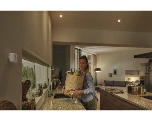 Femeie cu sacoșă de cumpărături în bucătărie sub spoturi de tavan și un senzor de mișcare.