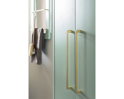 Prim-plan al unei băi cu un dulap cu două mânere aurii și un raft cu un prosop și o perie.