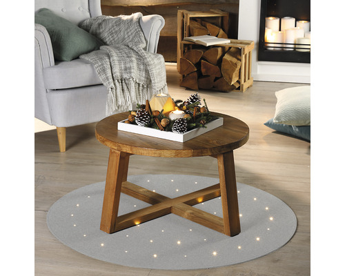 Living cu fotoliu, șemineu și măsuță de cafea rotundă pe un covor cu puncte de lumină