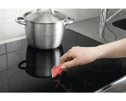 Curățarea unei plite cu un răzuitor lângă o oală