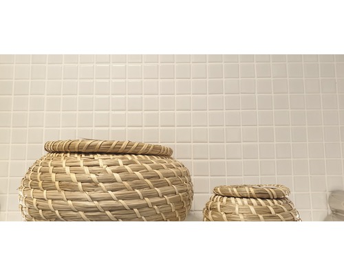 Două coșuri împletite cu capac în fața unui perete cu plăci pătrate mici.