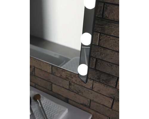 Detaliu cu o oglindă iluminată lângă un perete de cărămidă în baie