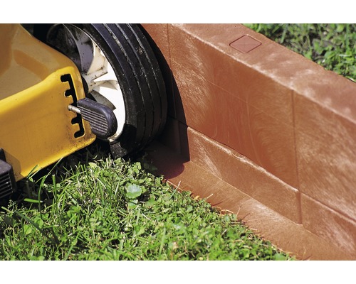 Prim-plan cu o mașină de tuns iarba lângă o margine de gazon.