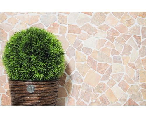 Plantă artificială decorativă în ghiveci în fața unui perete cu imitație de piatră