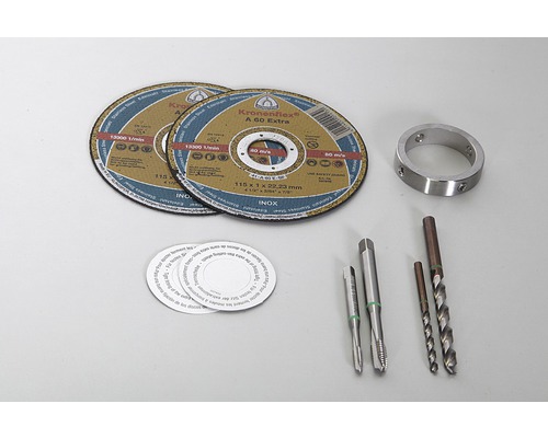 Două discuri de tăiere, un inel metalic, două tarozi, două burghie și mai multe autocolante rotunde sunt așezate pe o masă.