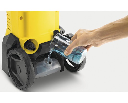 O persoană toarnă detergent într-un aparat de curățat cu presiune.