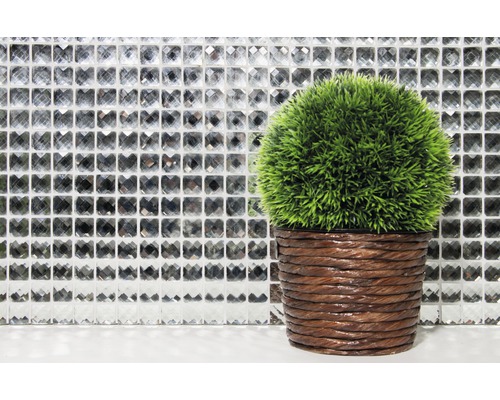 Plantă artificială verde decorativă în ghiveci maro în fața unui perete de mozaic