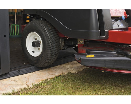 Mașină de tuns iarba cu scaun rulând pe o covorașă de cauciuc într-un garaj