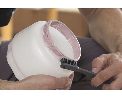 O persoană curăță o găleată de vopsea cu o perie.