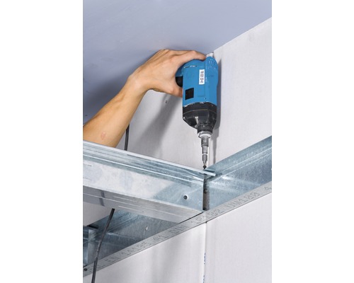 Un artizan fixează o placă de gips-carton pe o substructură metalică cu o șurubelniță cu acumulator.