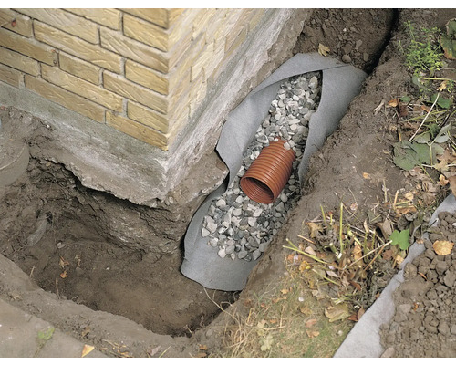 Șanț de drenaj cu tub de drenaj, pietriș și folie de protecție la fundația unei case.