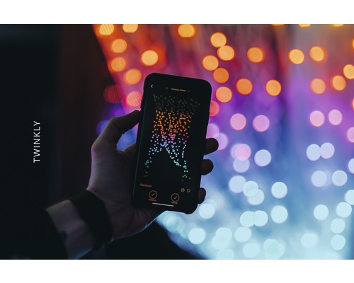 O mână ține un smartphone cu aplicația Twinkly în fața luminilor