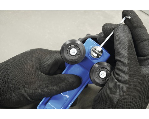 Prim-plan cu mâini în mănuși de lucru care reglează un tăietor de faianță albastru cu o cheie Allen.