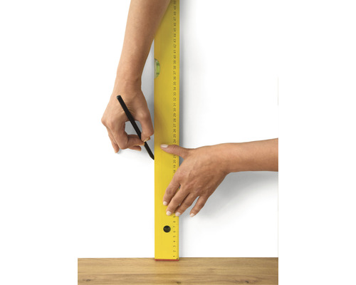 Persoană care trasează o linie cu creionul și bolobocul pe un perete.