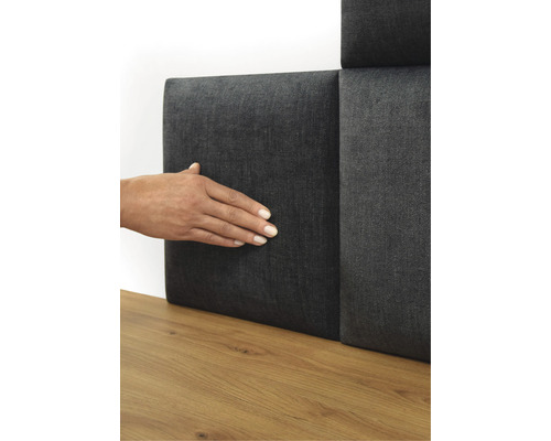 Persoană care atinge un panou de perete gri cu acoperire textilă pe o podea de lemn.