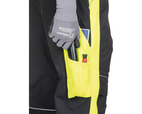 Detaliu al unor pantaloni de lucru cu scule în buzunar și o persoană cu mănuși de lucru