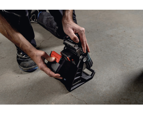 Vedere de sus a unei persoane care introduce o baterie într-o lampă de șantier Metabo.