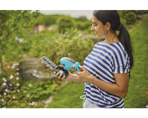 Femeie ținând în mână o foarfecă de iarbă cu acumulator Gardena cu lame interschimbabile.